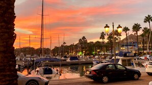 A marina with boats docked, a car parked, and a sunset in the background. - Charming apartment / Precioso apartamento en la Marina del Puerto de Sotogrande. (San Roque)