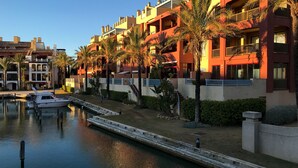 A waterfront hotel with multiple balconies, palm trees, and a dock with boats. - Charming apartment / Precioso apartamento en la Marina del Puerto de Sotogrande. (San Roque)