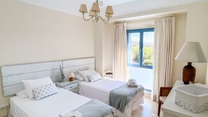 A hotel room with two beds, a nightstand, a lamp, a window with curtains, and a view of the outdoors. - Charming apartment / Precioso apartamento en la Marina del Puerto de Sotogrande. (San Roque)