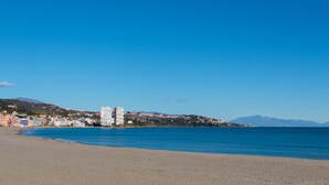 A beach with a clear sky, a sandy shore, and buildings in the background. - Charming apartment / Precioso apartamento en la Marina del Puerto de Sotogrande. (San Roque)