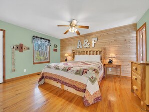 Une chambre à coucher avec une tête de lit en bois, un lit recouvert d’une courtepointe, un ventilateur de plafond et une commode en bois.