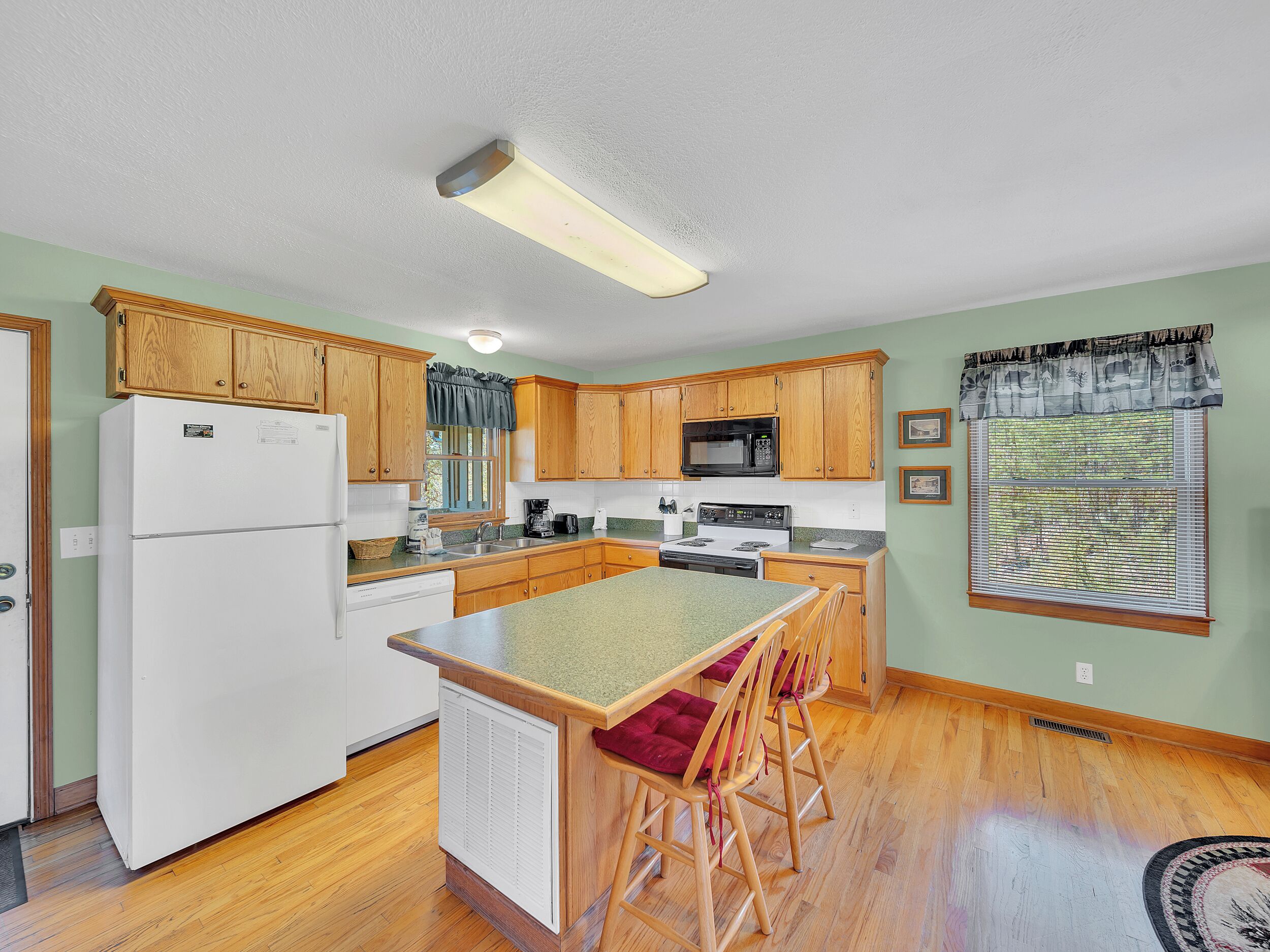 A kitchen with wooden cabinets, a refrigerator, a microwave, a stove, and a window with blinds.
