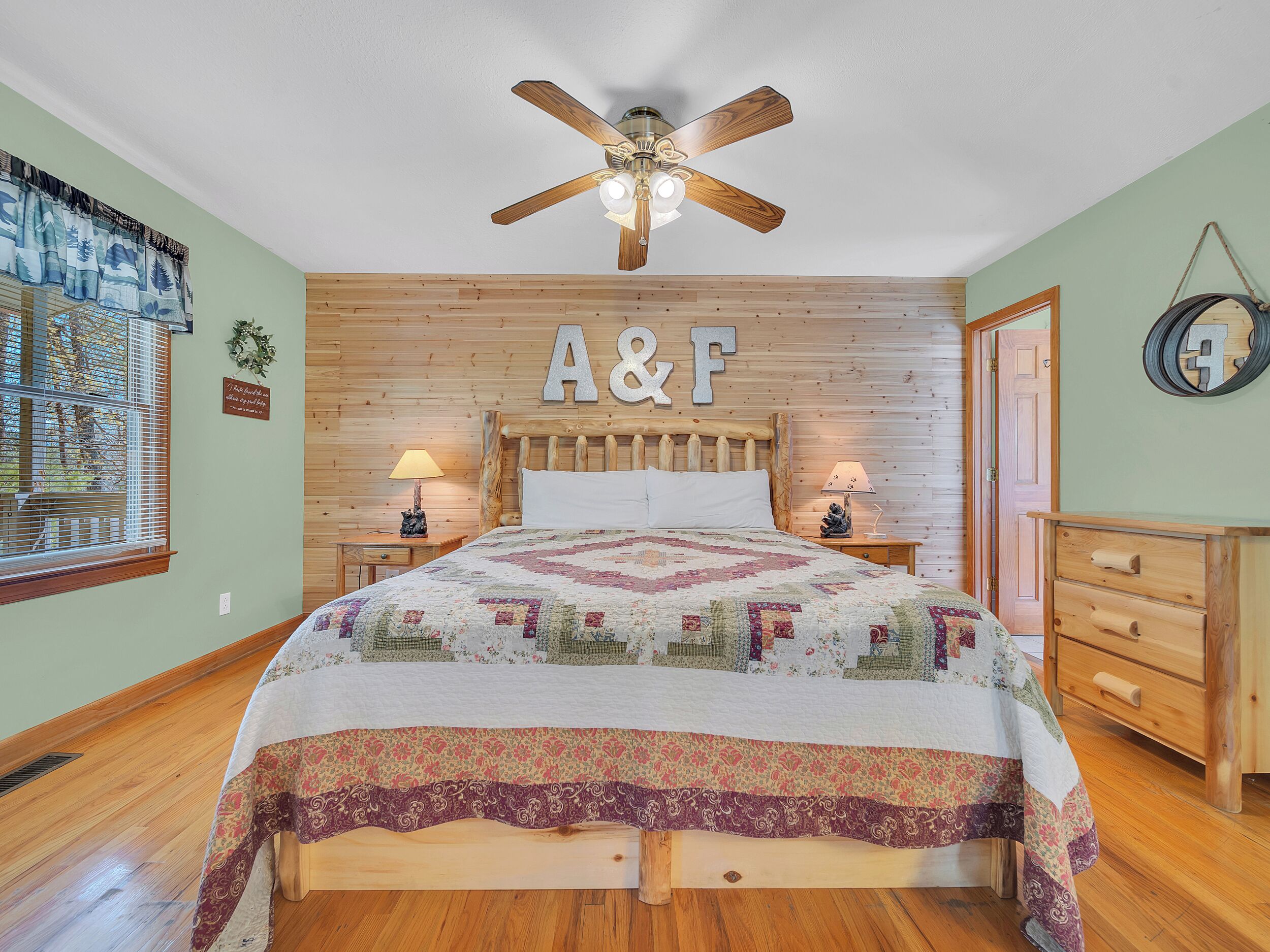 Une chambre à coucher avec une tête de lit en bois, une couvre-lit matelassée, deux lampes de chevet, un ventilateur de plafond et une commode en bois.
