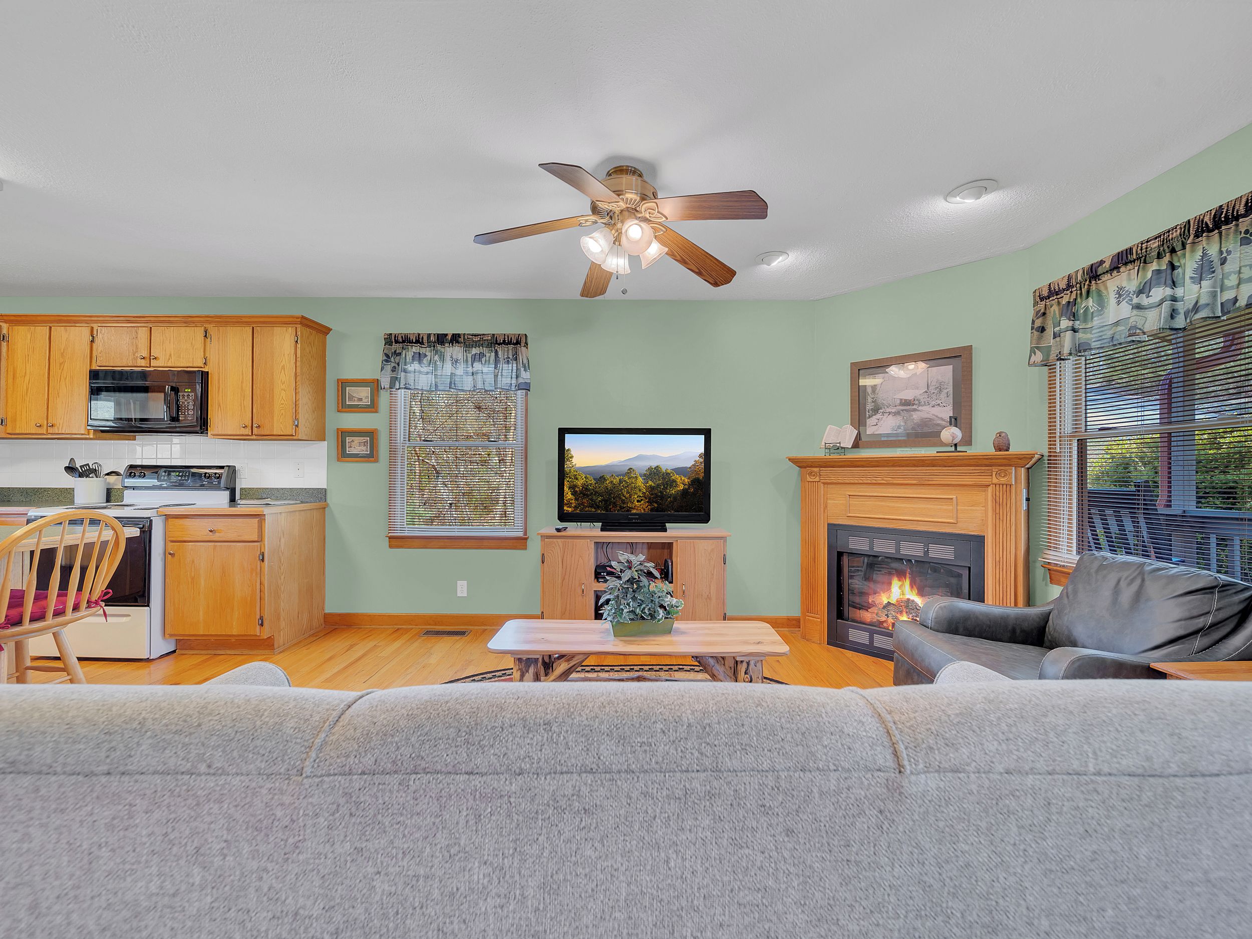 A living room with a fireplace, a television, and a kitchen area with wooden cabinets and a microwave.
