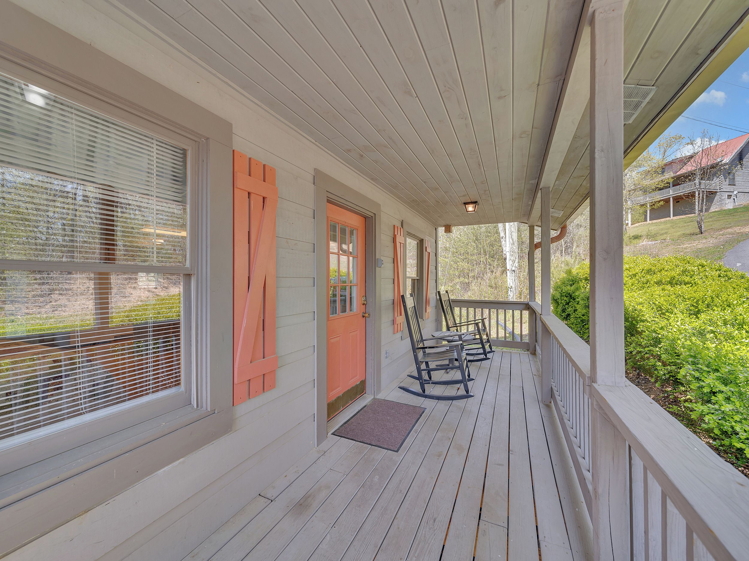 A covered porch with a wooden floor, a door with orange shutters, and a bench.