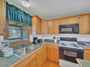 Une cuisine avec des meubles de rangement en bois, un évier en acier inoxydable, un four à micro-ondes et une cuisinière.