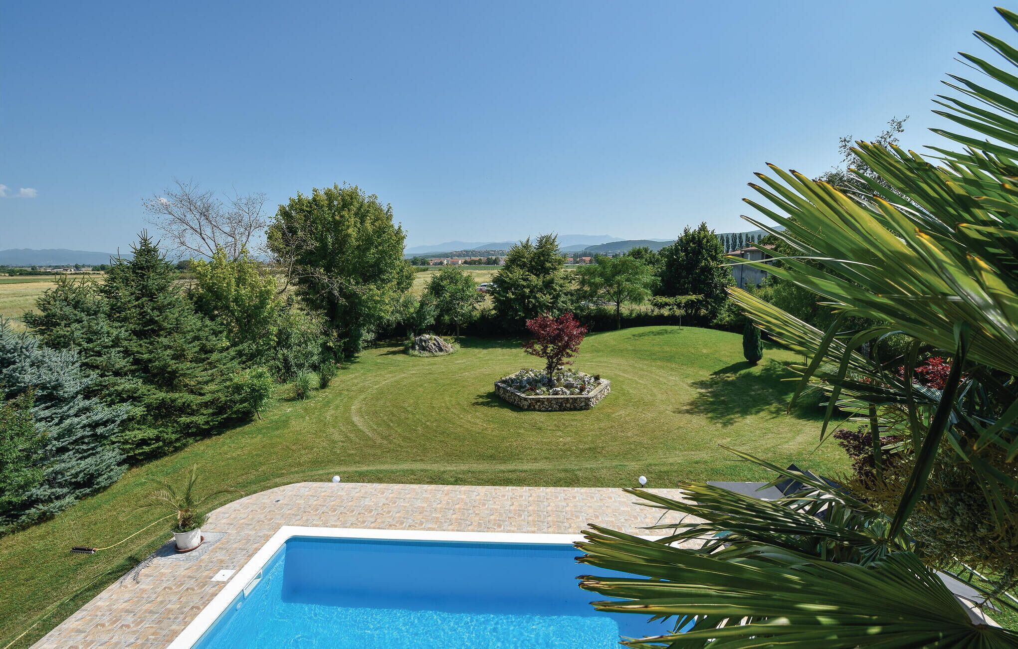 Una piscina con borde de piedra, rodeada de césped cuidado y varios árboles.