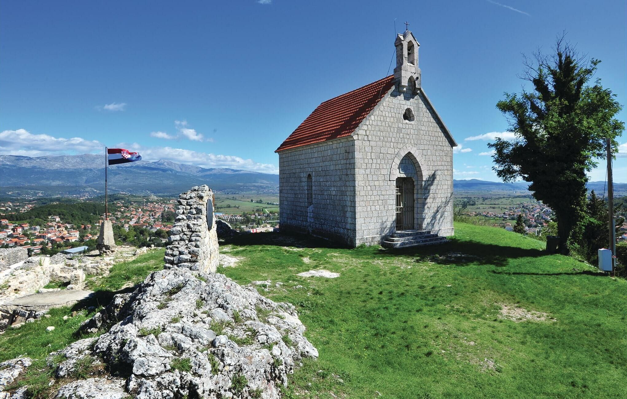 Una pequeña iglesia de piedra con techo rojo, rodeada de hierba verde y un muro de piedra.
