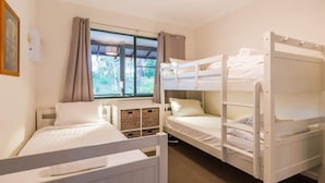 Une chambre avec des lits superposés, une fenêtre avec des rideaux et un petit meuble de rangement.