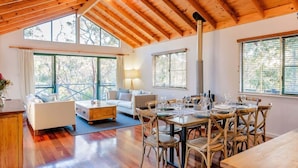 Une pièce spacieuse avec un plafond en bois, de grandes fenêtres, une table à manger avec des chaises et un canapé.
