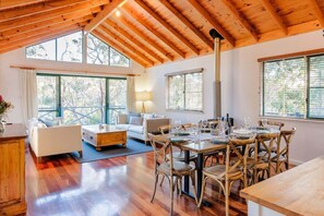 A spacious room with a wooden ceiling, large windows, a dining table with chairs, and a sofa.