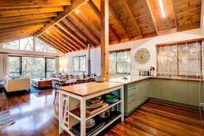 A spacious living area with wooden beams, a kitchen with a green cabinet, and large windows.