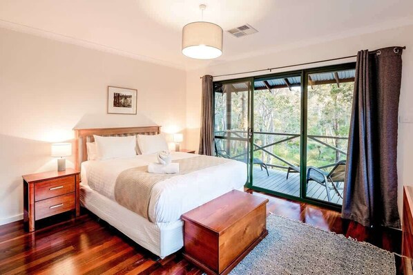A bedroom with a large bed, bedside tables, a wooden bench, and a view through a glass door to an outdoor deck.