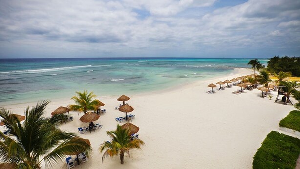 Une plage de sable blanc, avec une eau turquoise et limpide, et des parasols en chaume.