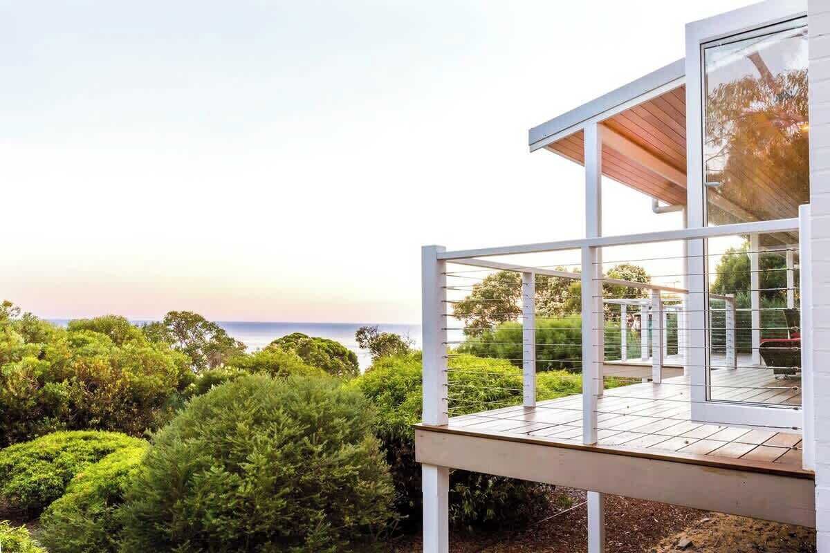 A modern house with a deck overlooking a garden and the ocean.