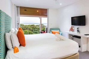 A hotel room with a bed, a desk, a TV, and a view of the sea. - The White House—Tranquil Sea Views and Endless Fun (Eagle Bay)