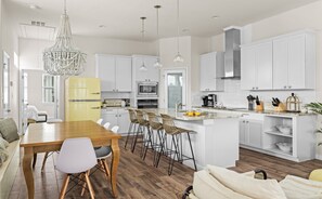 Una cocina moderna con armarios blancos, un refrigerador amarillo y un comedor con mesa y sillas de madera.