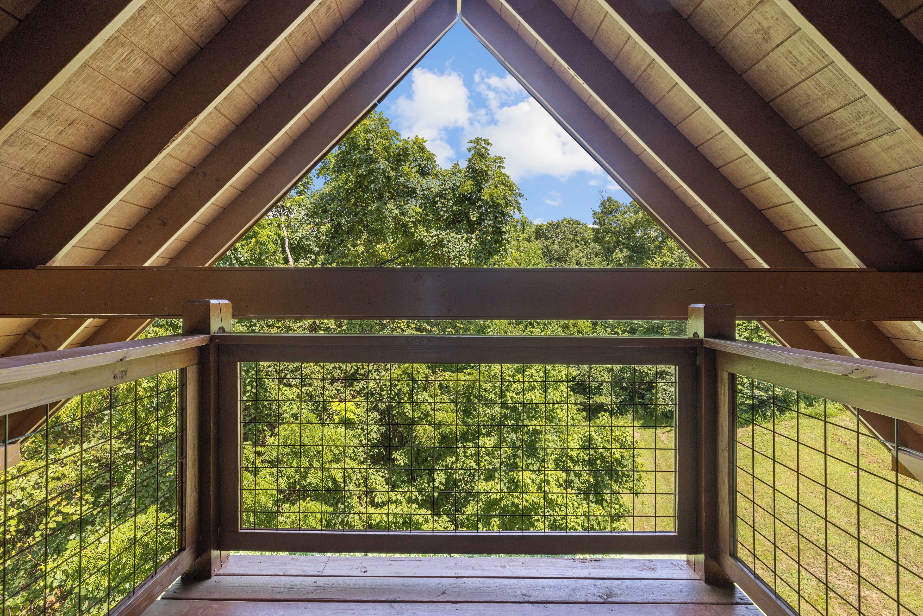 Een houten balkon met een metalen hekwerk met uitzicht op een dicht, groen bos.