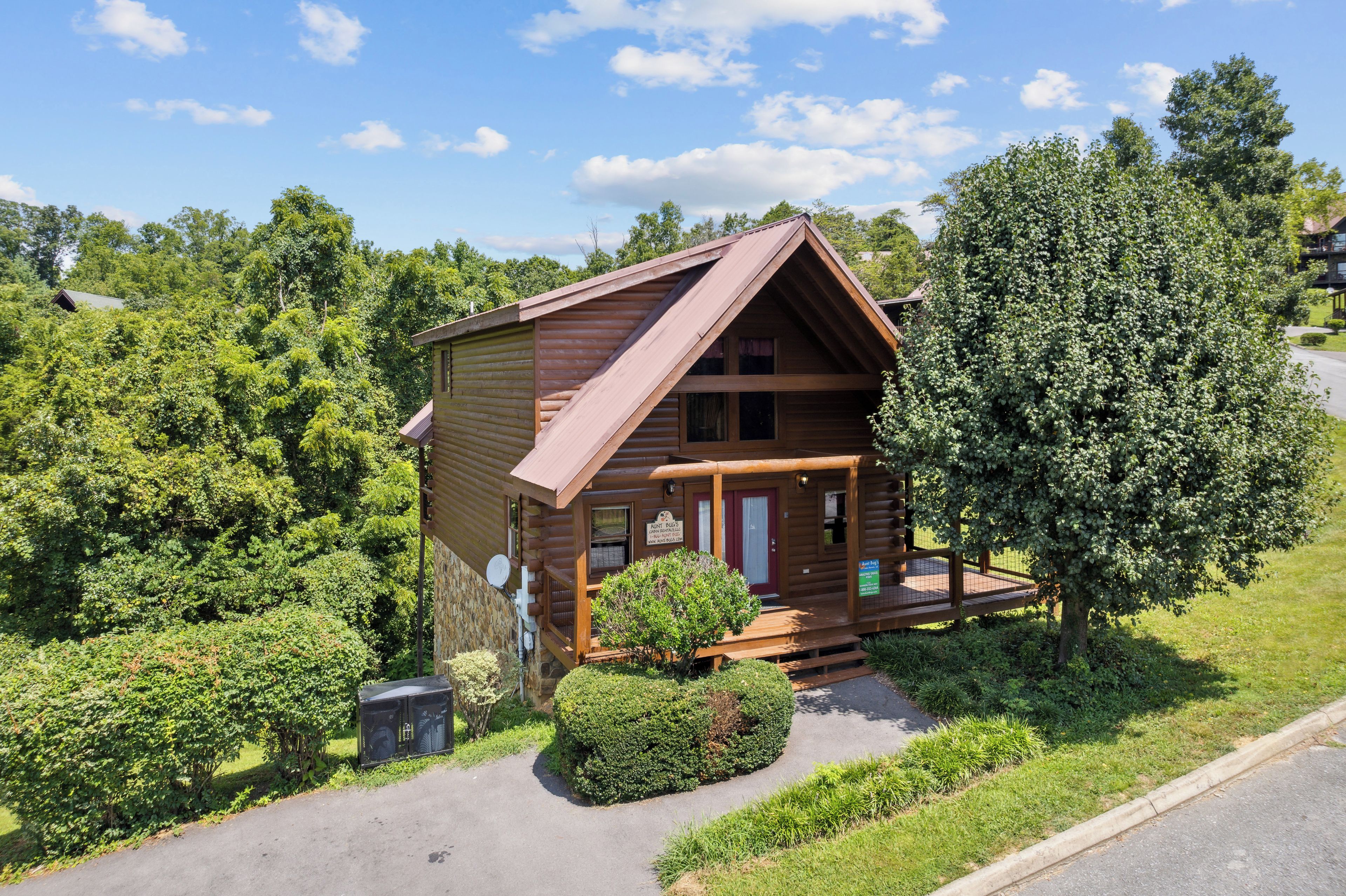 A wooden cabin with a porch, surrounded by lush greenery and trees.