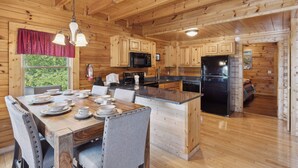 A wooden cabin kitchen with a dining table set for four, a microwave, a refrigerator, and a sink. - Cozy Cabin|2 King Suites w/Jacuzzis |Near Dollywood (SEVIERVILLE)