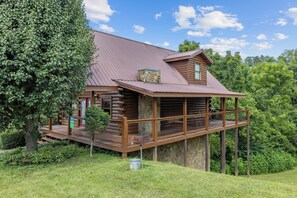 A log cabin with a balcony, surrounded by lush greenery. - Cozy Cabin|2 King Suites w/Jacuzzis |Near Dollywood (SEVIERVILLE)