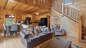 A wooden cabin interior with a dining area, a sofa, a chair, and a staircase. - Cozy Cabin|2 King Suites w/Jacuzzis |Near Dollywood (SEVIERVILLE)