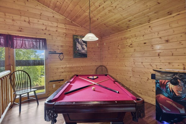 A pool table in a wooden room with a window and a poster on the wall.