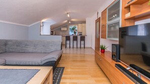 Ett modernt vardagsrum med en soffa, ett soffbord, en TV och en köksdel med ett matbord och stolar.