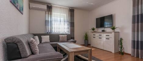 Un salón moderno con un sofá gris, una mesa de centro de madera y un televisor sobre un mueble.