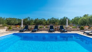 En swimmingpool med solstolar och parasoller, omgiven av grönska och krukväxter.