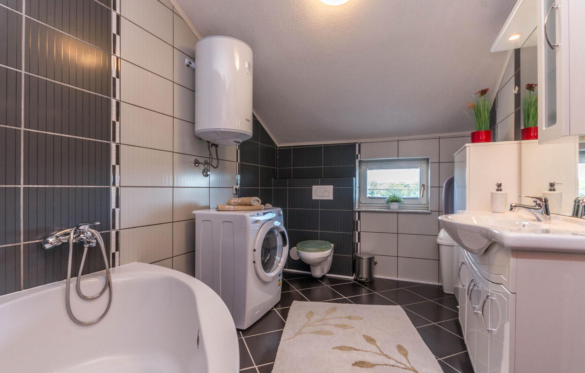 A compact bathroom with a bathtub, washing machine, toilet, and sink.
