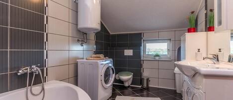 A compact bathroom with a bathtub, washing machine, toilet, and sink.