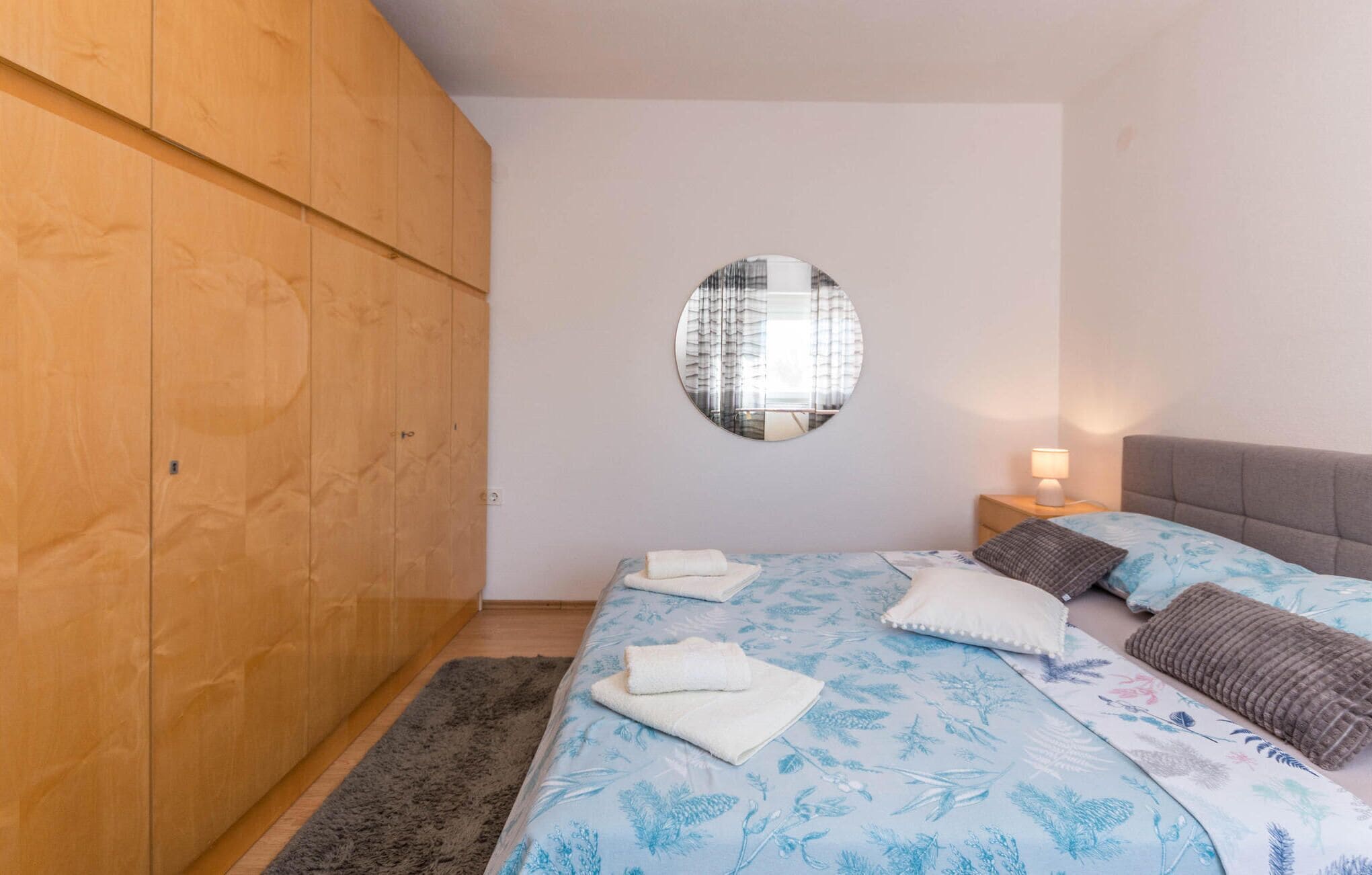 Ein Schlafzimmer mit einem Bett, einem runden Spiegel, einem Kleiderschrank und einem Nachttisch mit einer Lampe.