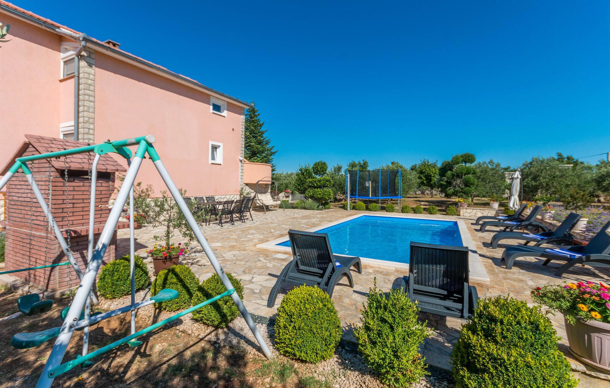 A swimming pool with lounge chairs, a swing set, and a patio area with a table and chairs.