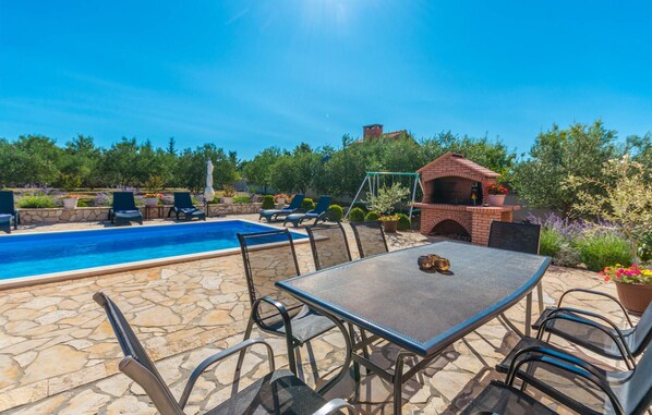 A pool area with a table and chairs, a brick barbecue, and surrounding greenery. - Stunning home in Miranje with private swimming pool, can be inside or outside (Miranje)