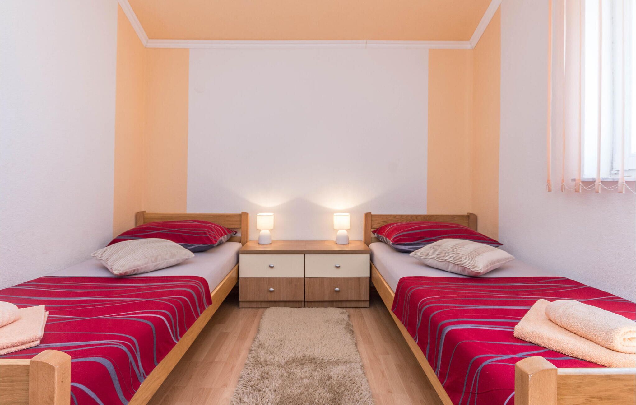 Une petite chambre à coucher accueillante, avec deux lits simples, une table de chevet dotée de deux lampes et un tapis moelleux sur le sol.