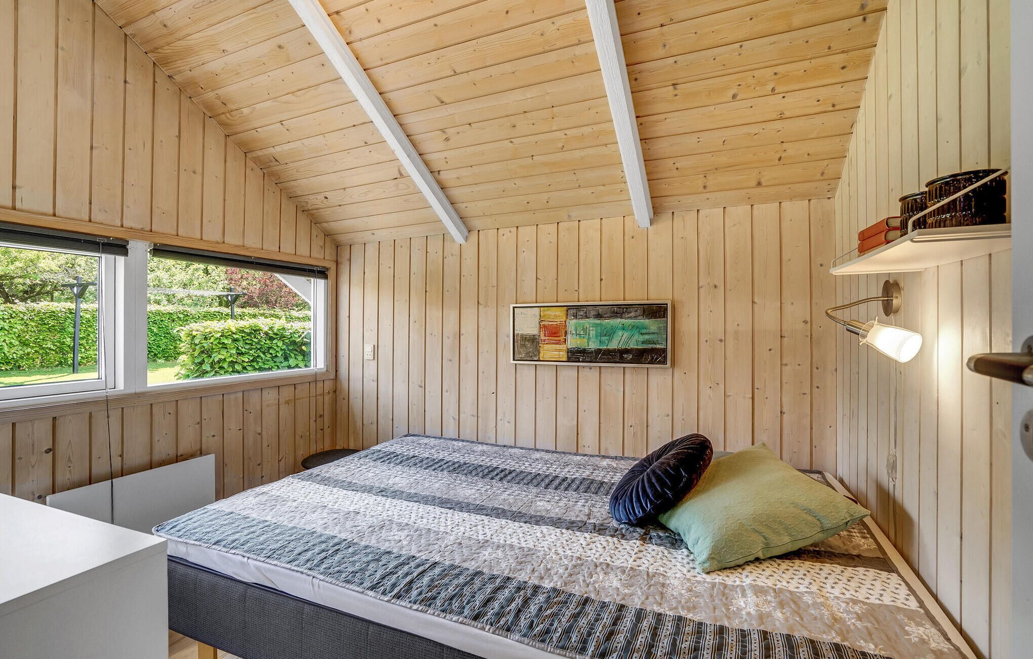 Una habitación con paneles de madera, una cama, un ventanal y un estante en la pared.
