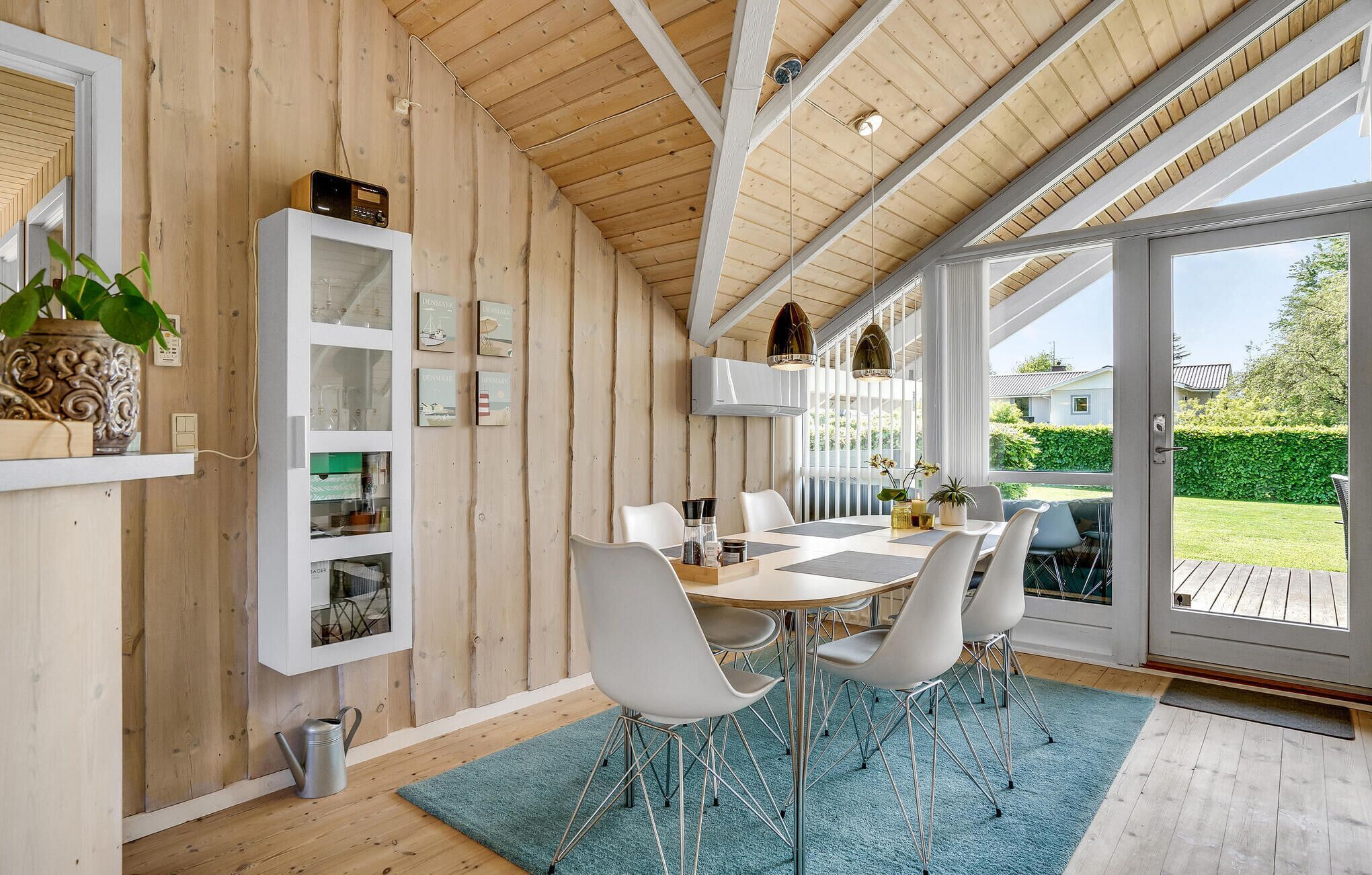 Zona pranzo moderna con finiture in legno, sedie bianche, un tavolo in vetro e vista sull'esterno.