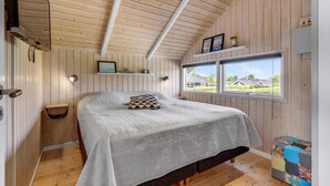 Et hyggeligt soveværelse med en stor seng, trævægge, et vindue med udsigt og en reol med dekorative genstande.
