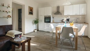 Ein modernes Wohnzimmer mit einer braunen Ledersofa, einem Holztisch und einem Essbereich mit einem Holztisch und weißen Stühlen. Im Hintergrund ist eine Küche mit weißen Schränken und Edelstahlgeräten zu sehen.
