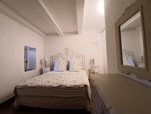 A bedroom with a bed, a dresser, a mirror, and a nightstand with a lamp.