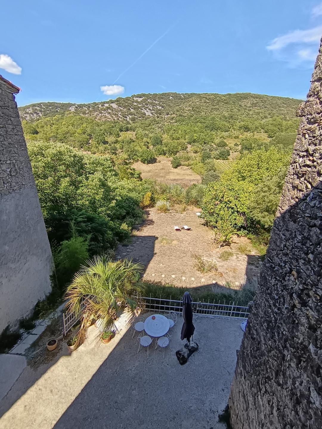 A terrace with a view of a green valley and hills, outdoor seating, and a stone wall.