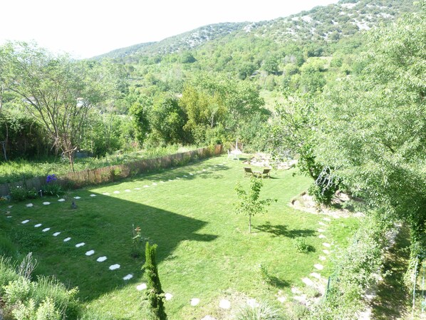 Un espacio al aire libre con césped, un sendero de piedra, un árbol pequeño y vistas a un paisaje montañoso.