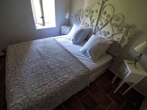 Una cama bien hecha con una colcha estampada, un cabecero blanco y una mesita de noche con una lámpara.
