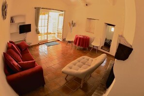 Un salón con un sofá rojo, un sillón blanco, un televisor y una mesa de comedor con mantel rojo.