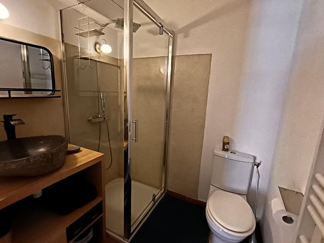 Un baño con ducha envuelta en vidrio, un tocador de madera con lavabo y un inodoro.