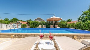 Una piscina con sillas de descanso y una mesa con copas de vino.