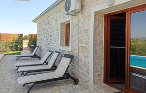 Un bâtiment en pierre doté d’une piscine, de chaises longues extérieures et d’un ventilateur fixé au mur.