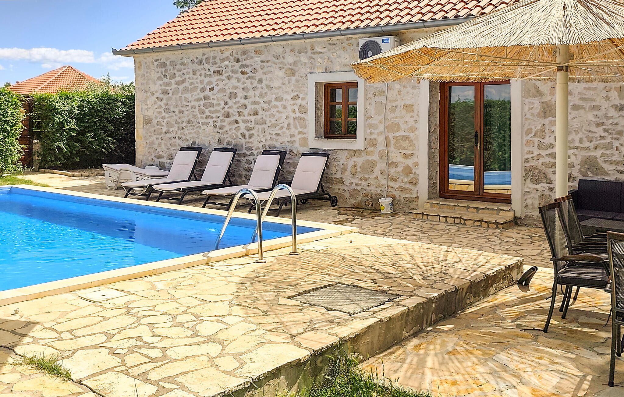 A stone building with a swimming pool, lounge chairs, and a covered seating area.