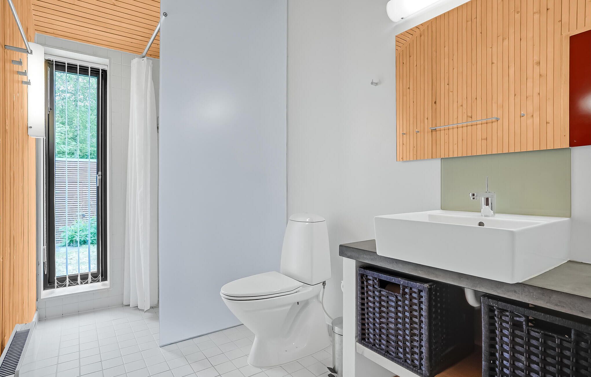 A modern bathroom with a white toilet, a white sink, and wooden cabinets.